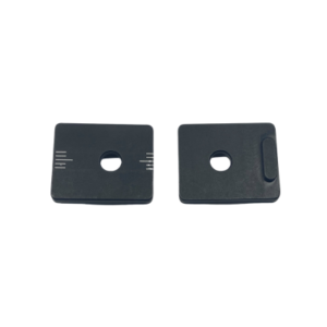 Two rectangular black parts with central holes and small white markings, one with an additional indented edge. These are likely components for a mechanical or electronic device named Rear Axle Cassette System - Pill Covers by Axiom.