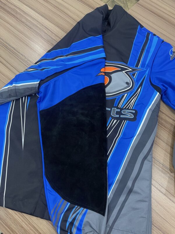 A SLACK Driving Jacket in blue and gray with a black patch on the sleeve and a logo design featuring an abstract bird on the chest, laid flat on a wooden surface.