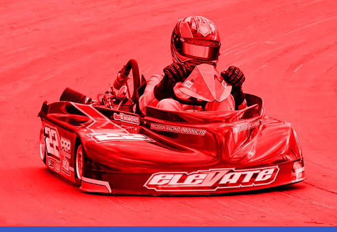 Person driving a go-kart on a track, wearing a helmet and racing suit. The image has a red overlay.